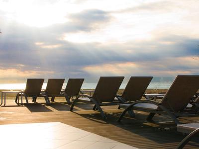 Lettini vuoti su un pontile in legno di fronte all'oceano sotto un cielo nuvoloso al tramonto.
