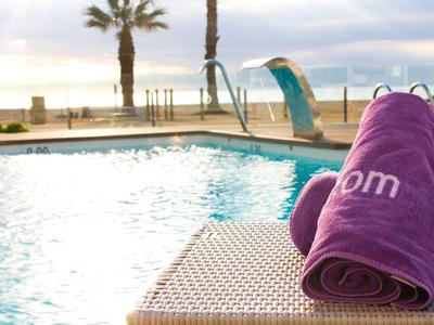 A pool with turquoise water and two purple towels on a lounge chair by the beach at sunset.
