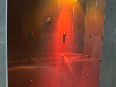 Doccia moderna con piastrelle scure strutturate e illuminazione rossa.