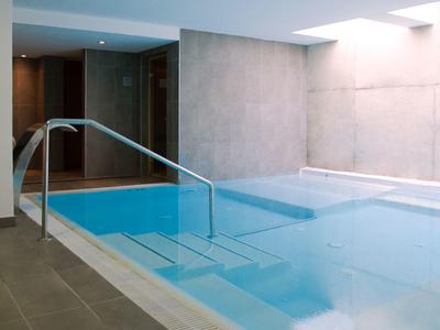 Piscina interna con ringhiera in vetro e scalini in una spa moderna.