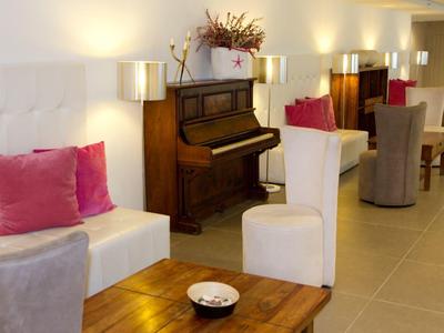 Area lounge accogliente con sedie bianche e grigie, pianoforte in legno e illuminazione soffusa.