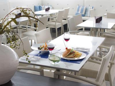 Area pranzo interna con tavoli bianchi, sedie e cibo con bevande su un tavolo.