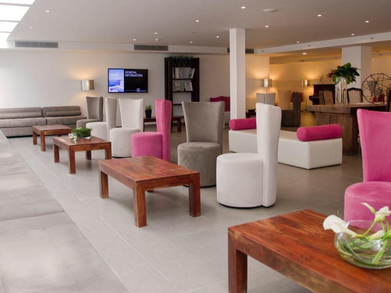 Moderna hall dell'hotel con divani bianchi, poltrone rosa e bianche, tavoli in legno e illuminazione luminosa.