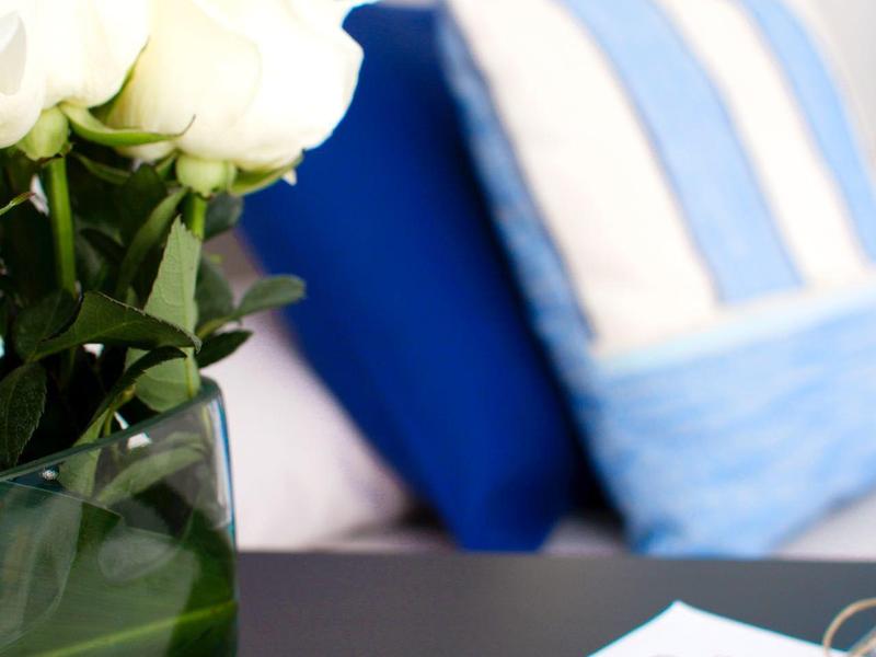 Rose bianche in vaso di vetro su tavolo con cuscini blu e bianchi sfocati sullo sfondo