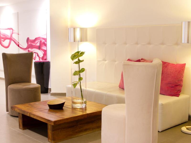 Accogliente salotto dell'hotel con illuminazione soffusa, divani beige, tavolo in legno e cuscini rosa decorativi.