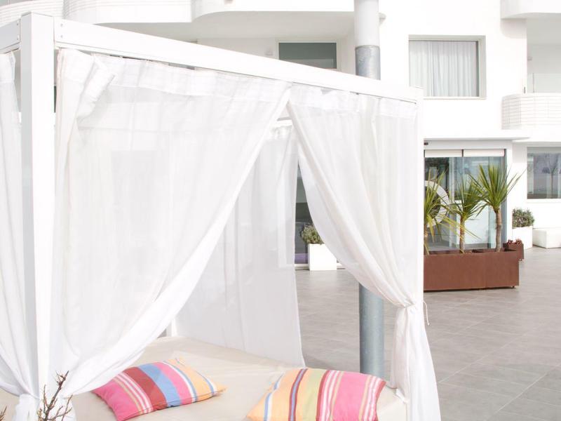 Letto da esterno bianco con cuscini colorati davanti a un edificio bianco moderno.