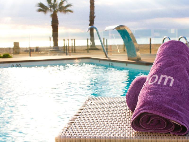 Asciugamani viola su sedia a sdraio a bordo piscina con palme e mare sullo sfondo al tramonto.