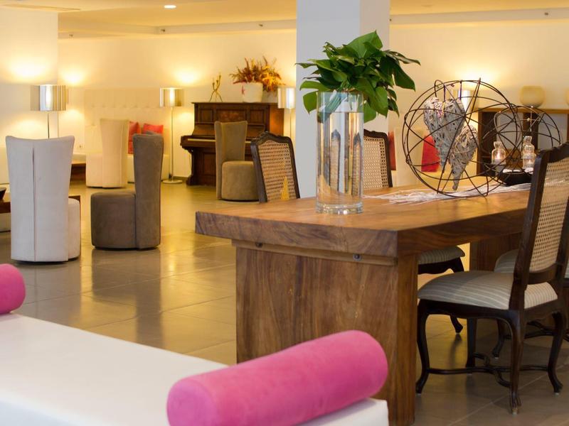 Accogliente hall d'hotel con tavolo in legno, sedie, sedute imbottite e illuminazione calda.