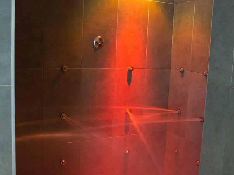 Doccia moderna con piastrelle scure strutturate e illuminazione rossa.