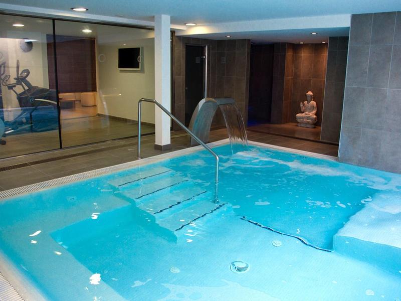 Piscina spa interna con acqua azzurra chiara, getti idromassaggio e pareti in legno con opere serene.