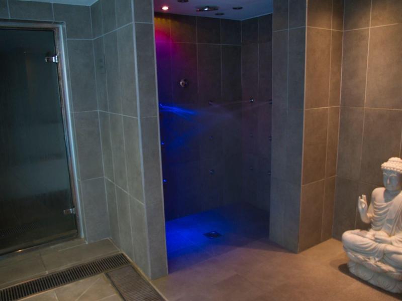 Una stanza SPA poco illuminata con una statua di Buddha in pietra e una porta di vetro per il bagno di vapore.