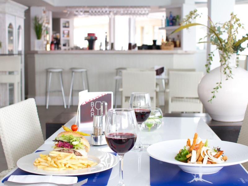 Tavolo da pranzo con pasta, insalata e bicchieri di vino in una cucina moderna e luminosa.