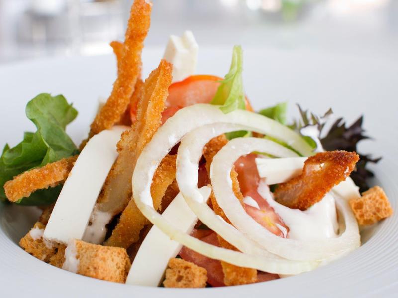 Insalata fresca con anelli di cipolla, fette di pomodoro, crostini e verdure miste in una ciotola bianca.
