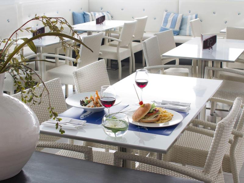 Area pranzo interna con tavoli bianchi, sedie e cibo con bevande su un tavolo.