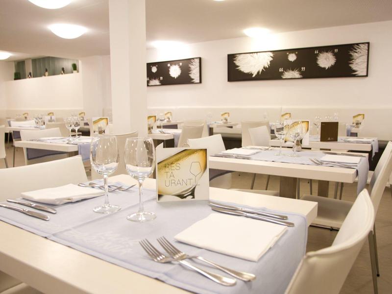 Area pranzo moderna con tavoli e sedie bianchi apparecchiati per gli ospiti in una stanza luminosa.