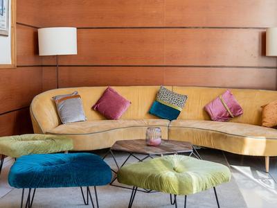 Sala acogedora con sofá amarillo, cojines de colores y pequeños taburetes acolchonados.