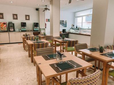 Sala de desayuno de hotel con mesas de madera y sillas con cojines de rayas.