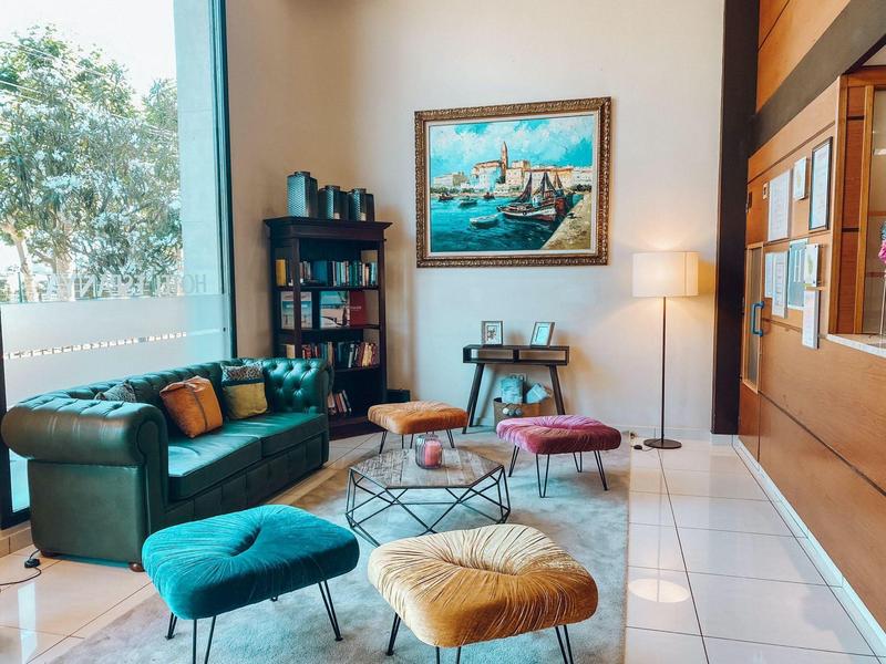 Sala de estar moderna con sofá verde, sillones coloridos y gran ventana con vista a árboles.