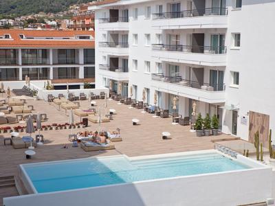 Moderner Hotelpool mit Liegestühlen auf einer großen Terrasse und umliegenden Gebäuden.