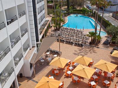 Hotelterrasse mit orangefarbenen Sonnenschirmen, Tischen und einem Pool im Hintergrund.