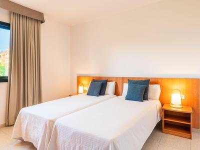 Helles Hotelzimmer mit zwei Einzelbetten, blauen Kissen und Nachttischlampen.