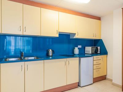 Moderne Küchenzeile mit blauer Glasrückwand, weißen Schränken und kleinen Geräten in einem Hotelzimmer.
