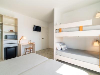 Helles Hotelzimmer mit Etagenbett, Doppelbett, Schreibtisch, Fernseher und Kleiderschrank.