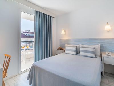 Helles Hotelzimmer mit Doppelbett, blau-weißen Vorhängen und Blick auf eine Terrasse.