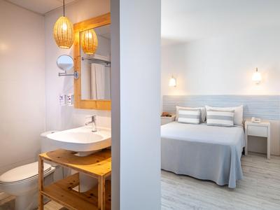 Hell eingerichtetes Hotelzimmer mit weißem Bett und modernem Bad mit Holzmöbeln.