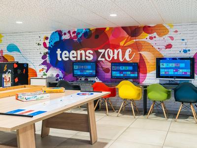Bunter Jugendbereich mit Computern, bunten Stühlen und einem Airhockey-Tisch in einem Hotel.