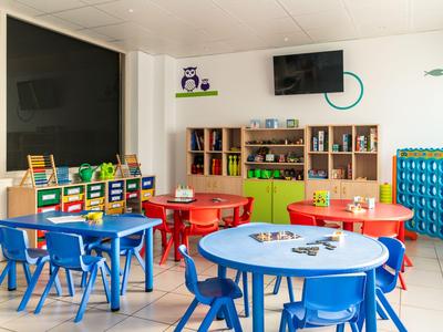 Bunt eingerichteter Kinderspielraum mit Tischen, Stühlen und Regalen in einem hellen Hotelbereich.