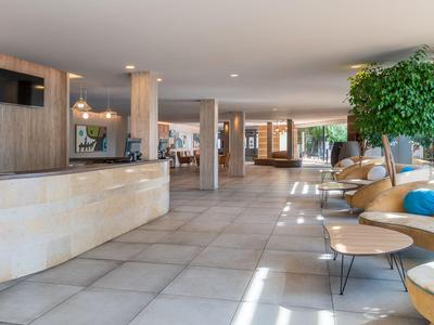 Heller Hotel-Lobbybereich mit Rezeption, Sitzgelegenheiten und großen Fenstern.