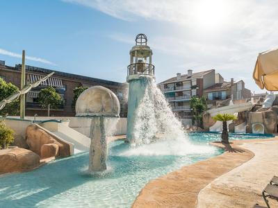Wasserfall in einem Hotelpool mit Felsen und Liegestühlen bei sonnigem Wetter.