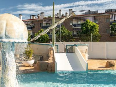 Kind wagt Sprung von Rutsche in Pool, umgeben von Wohngebäuden und klarem Himmel.