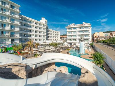 Hotel mit weißen Gebäuden, Sonnenschirmen und Außenpool unter blauem Himmel.