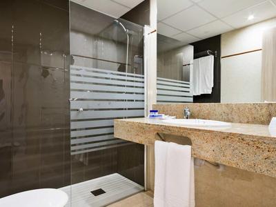 Modern bathroom with glass shower, beige countertop, towel, and bright lighting.