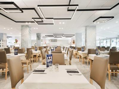 Spacious hotel dining area with modern lighting and beige chairs.