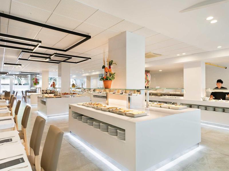 Modern hotel buffet area with sleek white counters, seating, and stylish lighting fixtures.