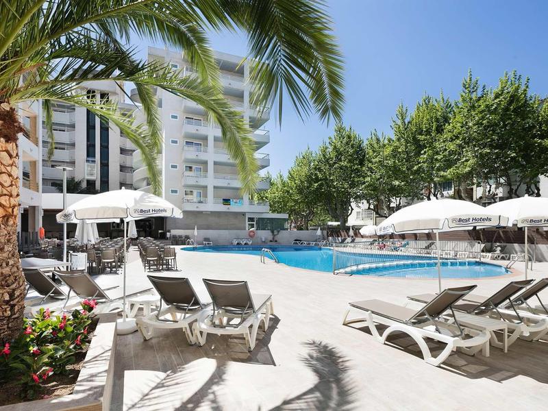 Sun loungers and umbrellas by a pool at a sunny hotel outdoor area with palm trees.
