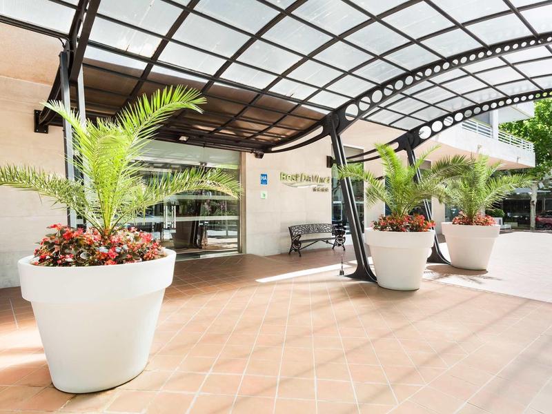 Hotel entrance with large white planters and tropical plants under a glass canopy