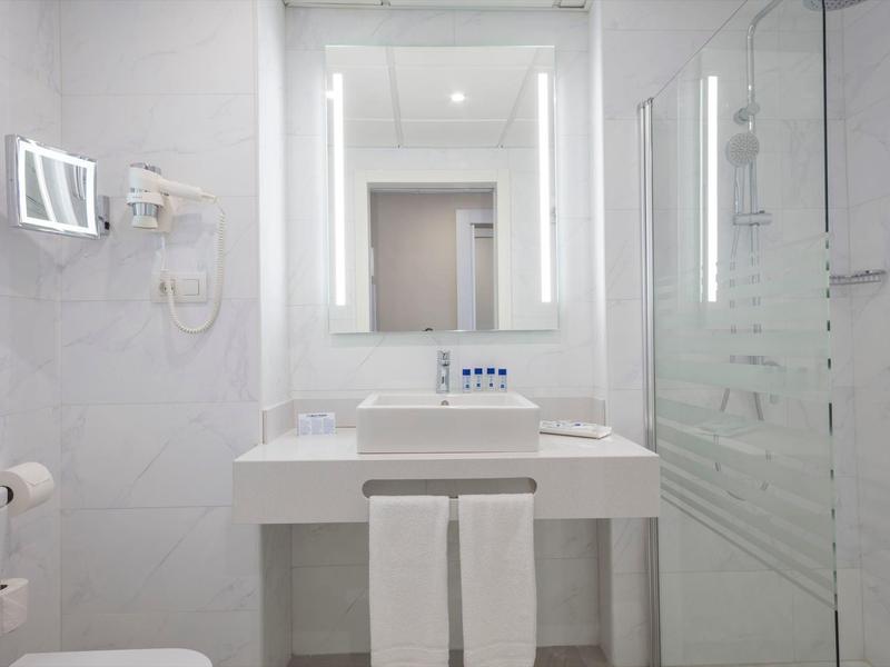 Moderní koupelna s umyvadlem, osvětleným zrcadlem a sprchovým koutem.