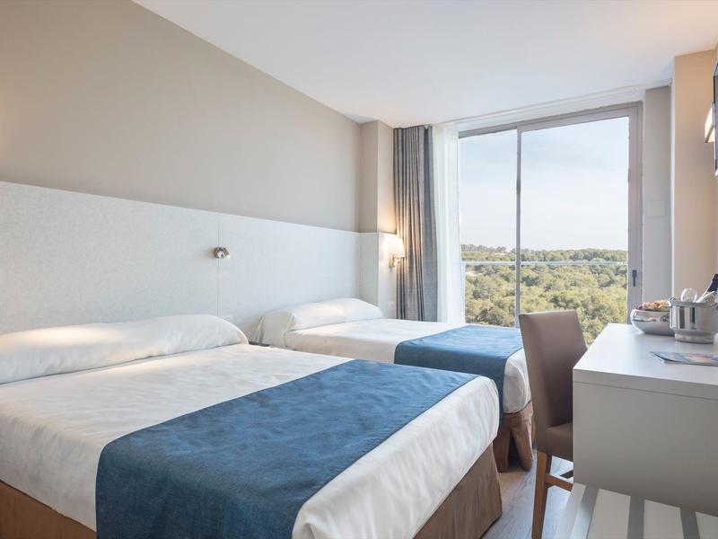 Světý hotelový pokoj se dvěma postelemi, psacím stolem a výhledem na zelenou krajinu.