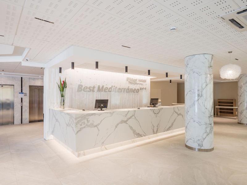 Moderní hotelová recepce s mramorovanou přepážkou a výtahy v pozadí.