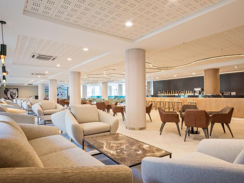 Světlý hotelový salonek s pohovkami, křesly a barem v pozadí.