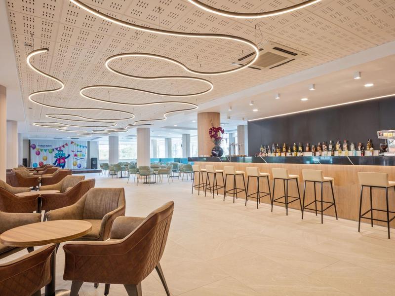 Světý interiér hotelového baru s moderními křesly a minimalistickým pultem.