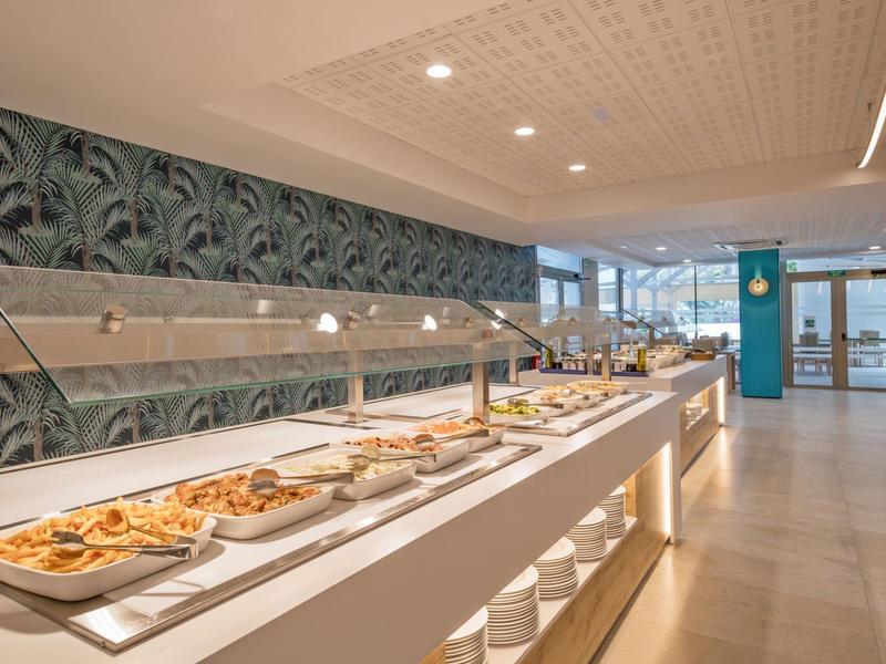 Bufet s různými pokrmy v moderní, světlé restauraci s velkými okny.