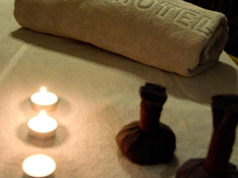 Handtuch mit "Gina Hotel" Schriftzug, drei brennende Kerzen und zwei Kräuterstempel auf weißem Tuch.