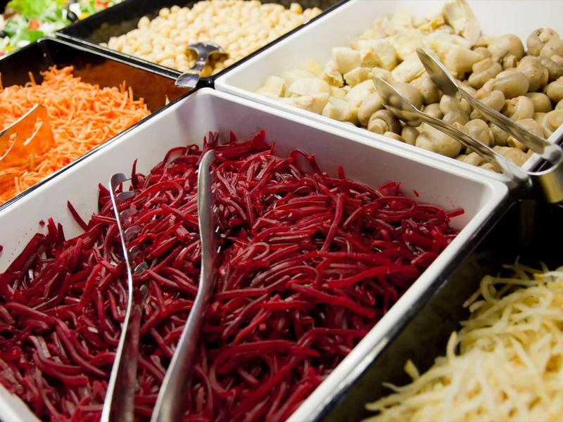 Mehrere weiße Schalen mit verschiedenen roten, orangen, gelben und weißen Gemüsesorten auf einem Buffet.