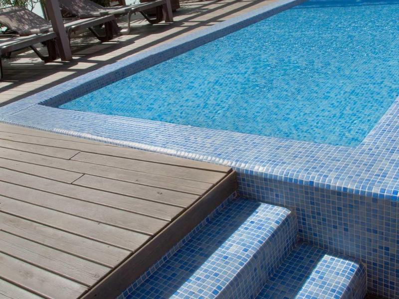 Ein blauer Pool mit drei Treppenstufen und einem Holzdeck an der Seite.
