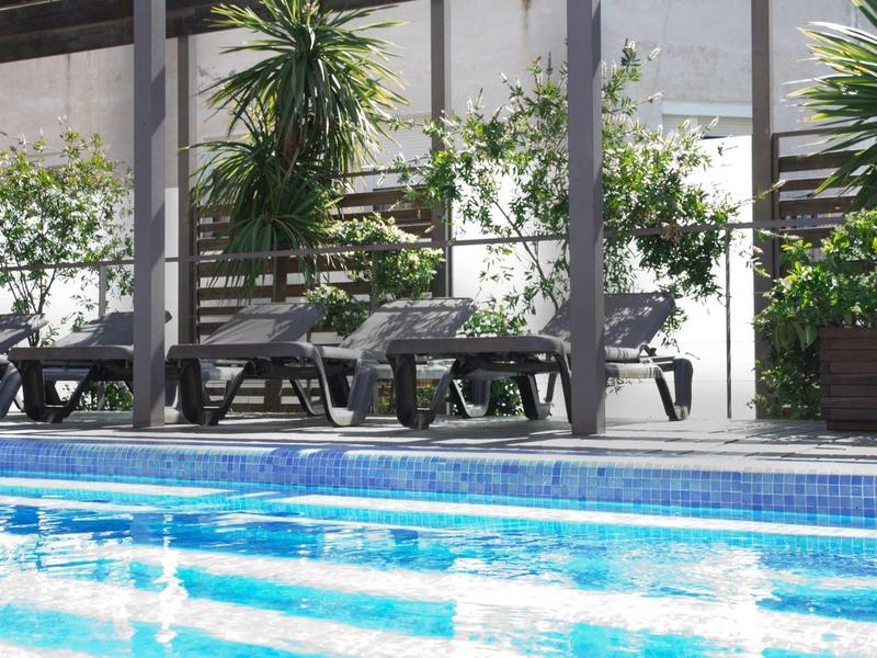 Schwimmbad mit blau schimmerndem Wasser, Liegestühlen und grünen Pflanzen am Rand.